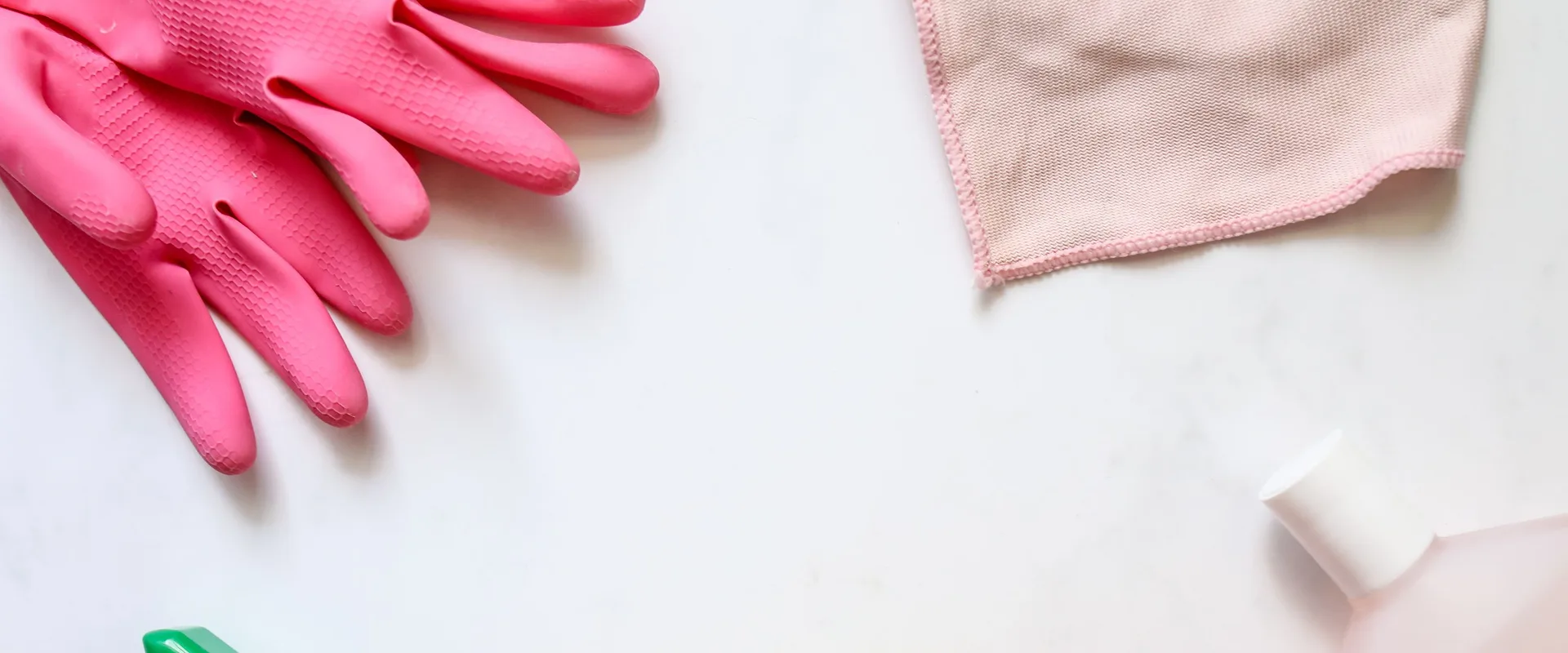 Pink cleaning gloves, a cleaning cloth, and a spray bottle laid out on a countertop