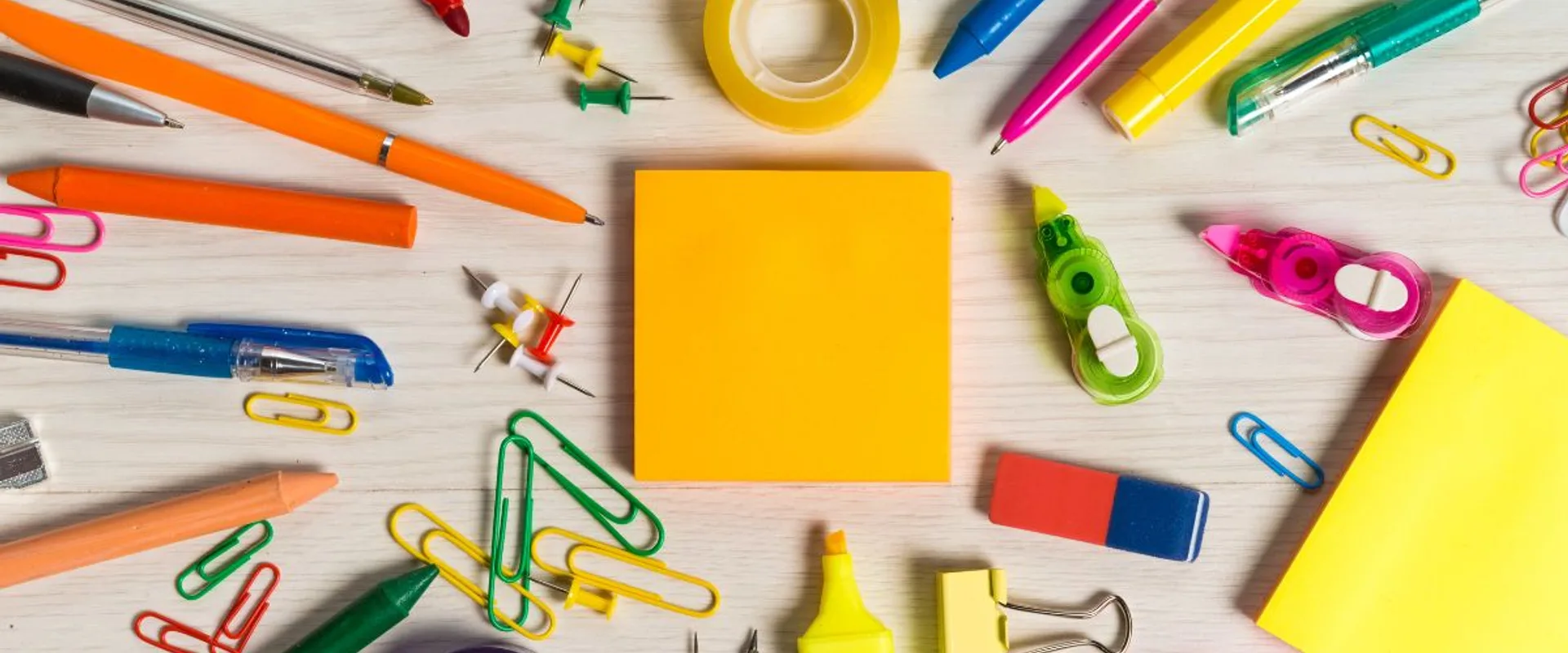 Colorful pens, pencils, sticky notes, paperclips, tape, and erasers laid out on a desk